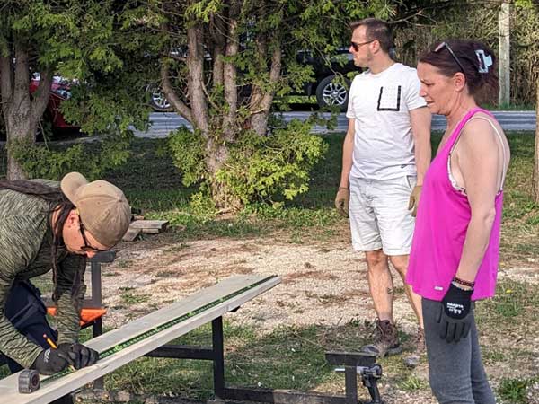 A volunteer measures wood while two others look on